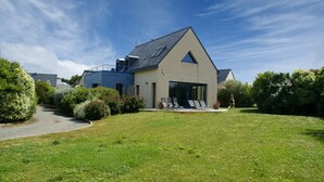 Une maison moderne dotée d’une grande pelouse, d’un espace extérieur aménagé et couvert, et d’un ciel dégagé.