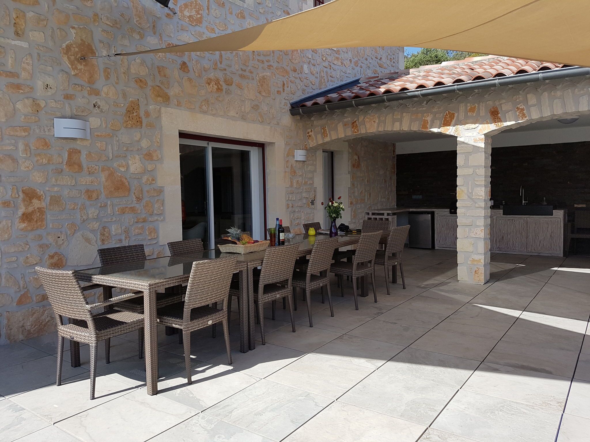 Un patio al aire libre con paredes de piedra, una mesa de comedor con sillas de mimbre y una zona de cocina.