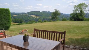 A wooden table with a potted plant, set outdoors with a view of a grassy field and hills in the background. - Vacation Home in France with Pool (Vaux)
