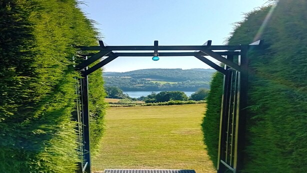 A metal archway leading to a grassy field with a view of hills and a body of water in the distance. - Vacation Home in France with Pool (Vaux)