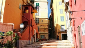 A narrow street with buildings on either side, featuring balconies and a staircase leading to an upper floor.