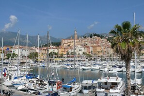 Una marina con numerose imbarcazioni ormeggiate, un edificio imponente con una torre sullo sfondo e un cielo sereno.