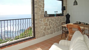 A balcony with a stone wall, a dining area with wicker furniture, and a view of the sea.