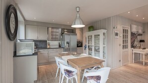 A modern kitchen with white cabinets, a wooden dining table, and white chairs. - Nice holiday home in Westende-Bad with sauna and pingpong (Westende)