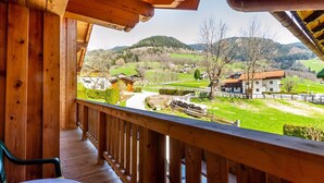 Un balcon en bois offrant une vue sur un paysage rural, avec des maisons et des collines.