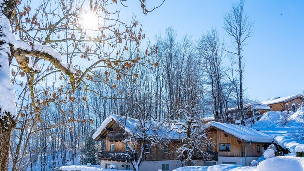 Une cabane en bois dotée d’un balcon, entourée d’arbres couverts de neige et surplombant un ciel dégagé.