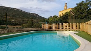 Une piscine entourée d’une clôture en bois, avec un bâtiment doté d’un clocher en arrière-plan.