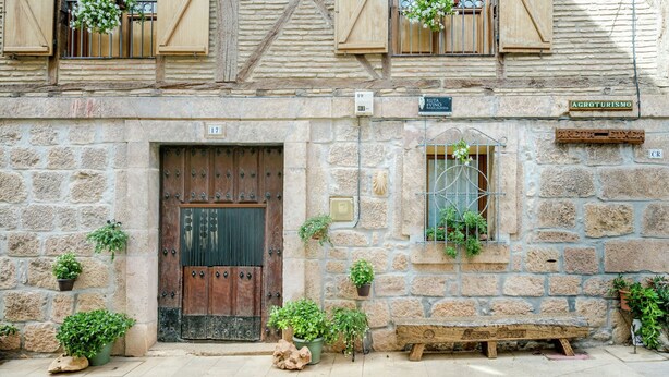 Un bâtiment en pierre avec une porte en bois, des plantes en pot et un banc à l’extérieur.