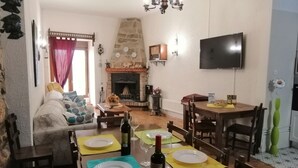 Un coin repas agrémenté d’une cheminée en pierre, d’un téléviseur fixé au mur et d’un canapé en arrière-plan.