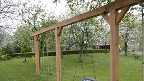 A wooden swing set in a park with a grassy area and trees.