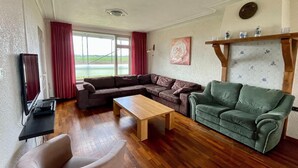 A living room with a sectional sofa, a green armchair, a wooden coffee table, and a television on a stand.
