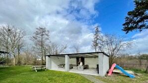 A modern outdoor pavilion with a fireplace, seating, and a slide.