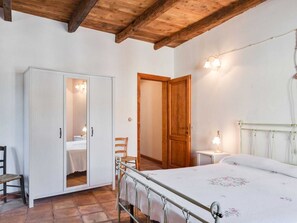 Un dormitorio con una cama, un armario, una silla y una mesita de noche con lámpara.