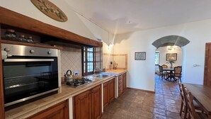 A kitchen with a built-in oven, a gas stove, wooden cabinets, and a stone floor.