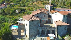 A stone building with a bell tower, surrounded by greenery and a swimming pool.