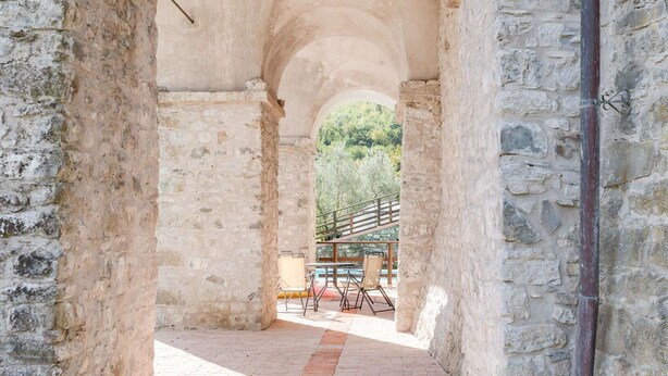 An arched stone corridor with a view of a pool area and outdoor seating.
