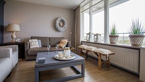 A modern living room with a sofa, coffee table, and a view of the outdoors through large windows.