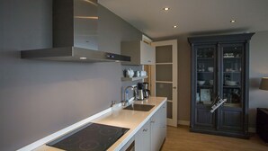 A modern kitchen with a built-in stove, a coffee maker, and a cabinet with glass doors.