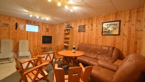Um quarto acolhedor com paredes de madeira, um sofá de couro marrom, cadeiras de madeira, uma mesa redonda e uma televisão.