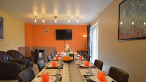 Uma sala de jantar com uma mesa comprida posta para refeição, uma lareira e uma televisão na parede.