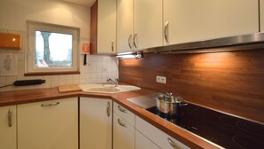 Cozinha com armários brancos, bancada de madeira, pia e fogão.