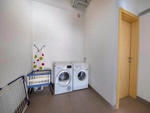 A laundry room with two washing machines, a drying rack, and a wooden door.