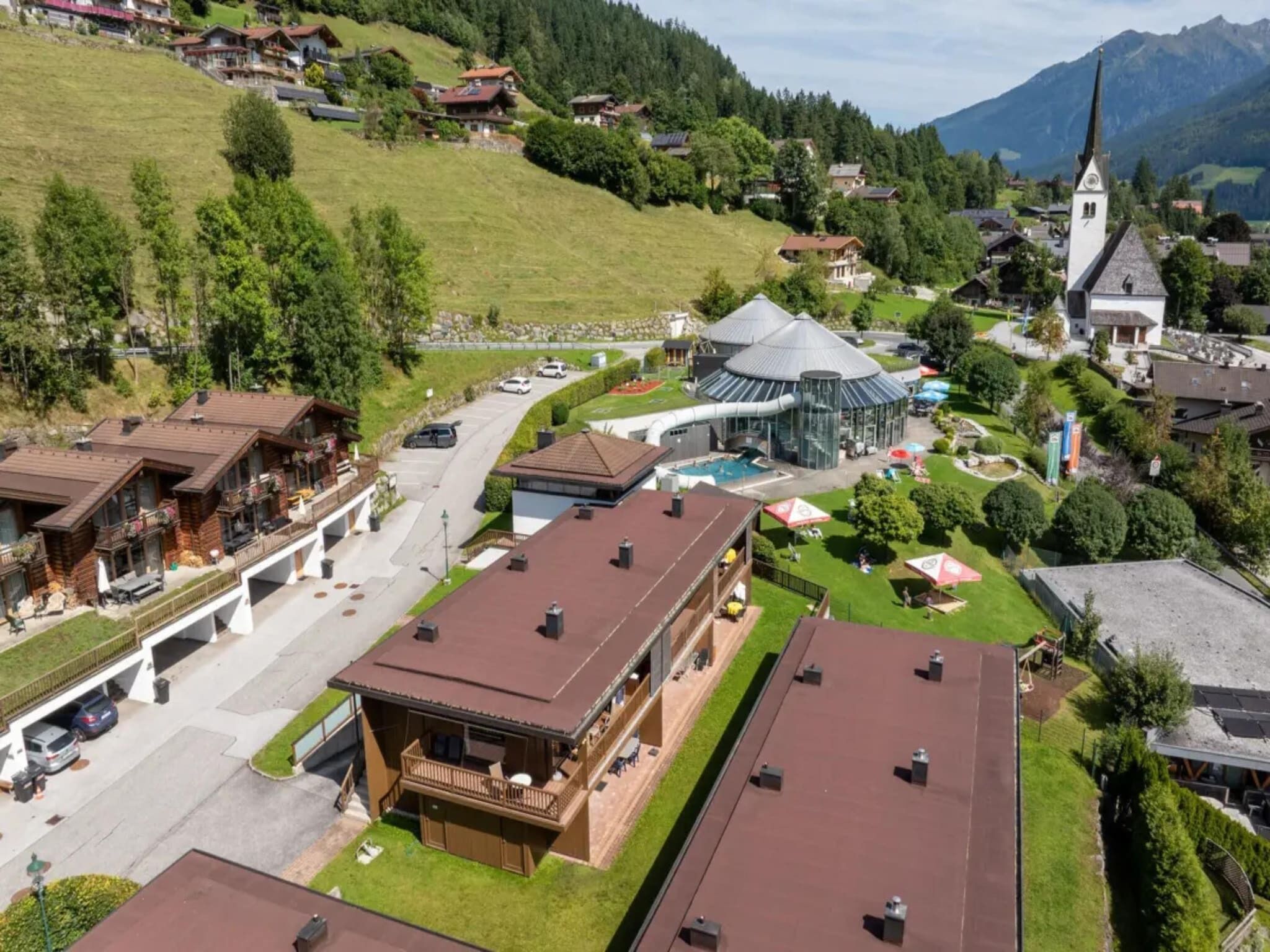 Un pueblo montañoso con casas tradicionales, una iglesia y un edificio moderno con piscina.