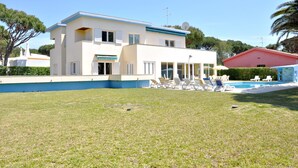 A two-story house with a swimming pool, outdoor seating, and a well-maintained lawn.