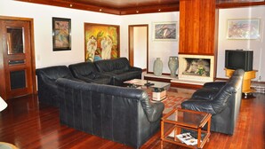 A living room with a black leather sofa, a coffee table, and a fireplace. There are paintings on the walls and a television on a stand.