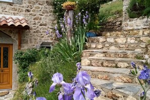 A stone building with a wooden door and steps leading up to a garden with purple flowers. - House in Ardèche near Ray-Pic Falls (Saint-Pierre-De-Colombier)