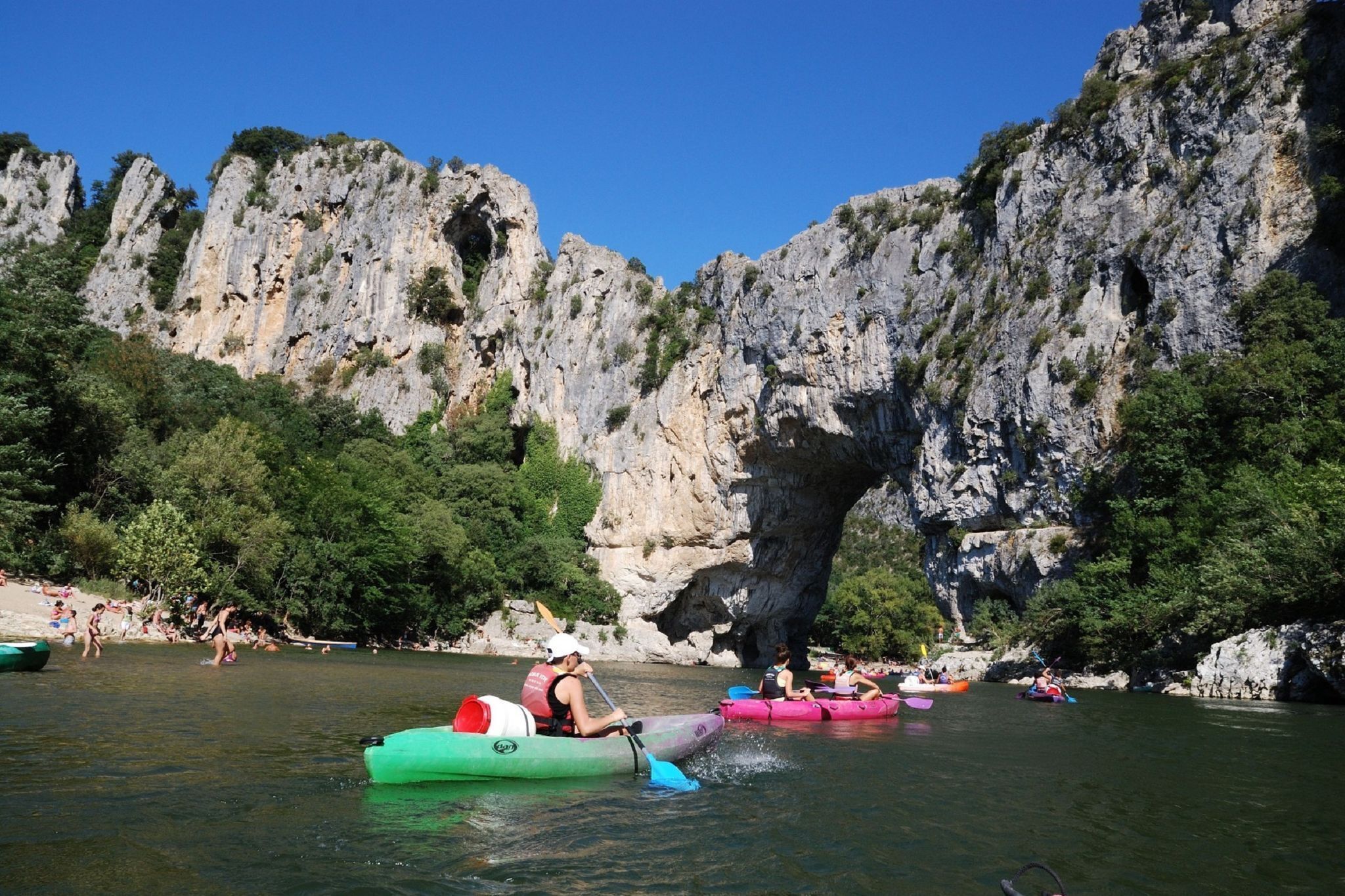 A group of people kayaking on a river with rocky cliffs in the background.