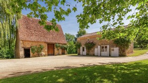 Een rustiek stenen gebouw met een pannendak, een grindpad en een gazon met bomen.