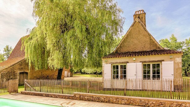 Een traditioneel huis met rieten dak, houten omheining en een zwembad.