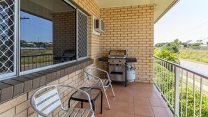 Een balkon met een barbecue, stoelen en uitzicht op de weg.
