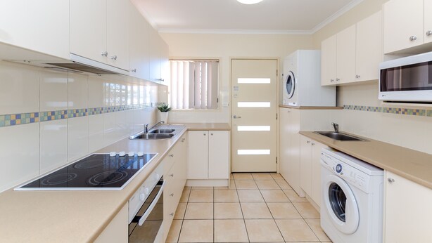 Een compacte keuken met een ingebouwde kookplaat, een wasmachine en een magnetron.