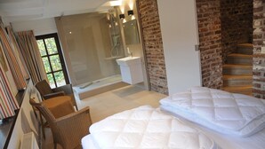 Une chambre moderne avec un grand lit, un coin salon avec un fauteuil, une douche en verre et un mur en briques.
