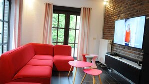 Un salon moderne avec un canapé rouge, un téléviseur fixé à un mur en briques et une fenêtre avec des rideaux.
