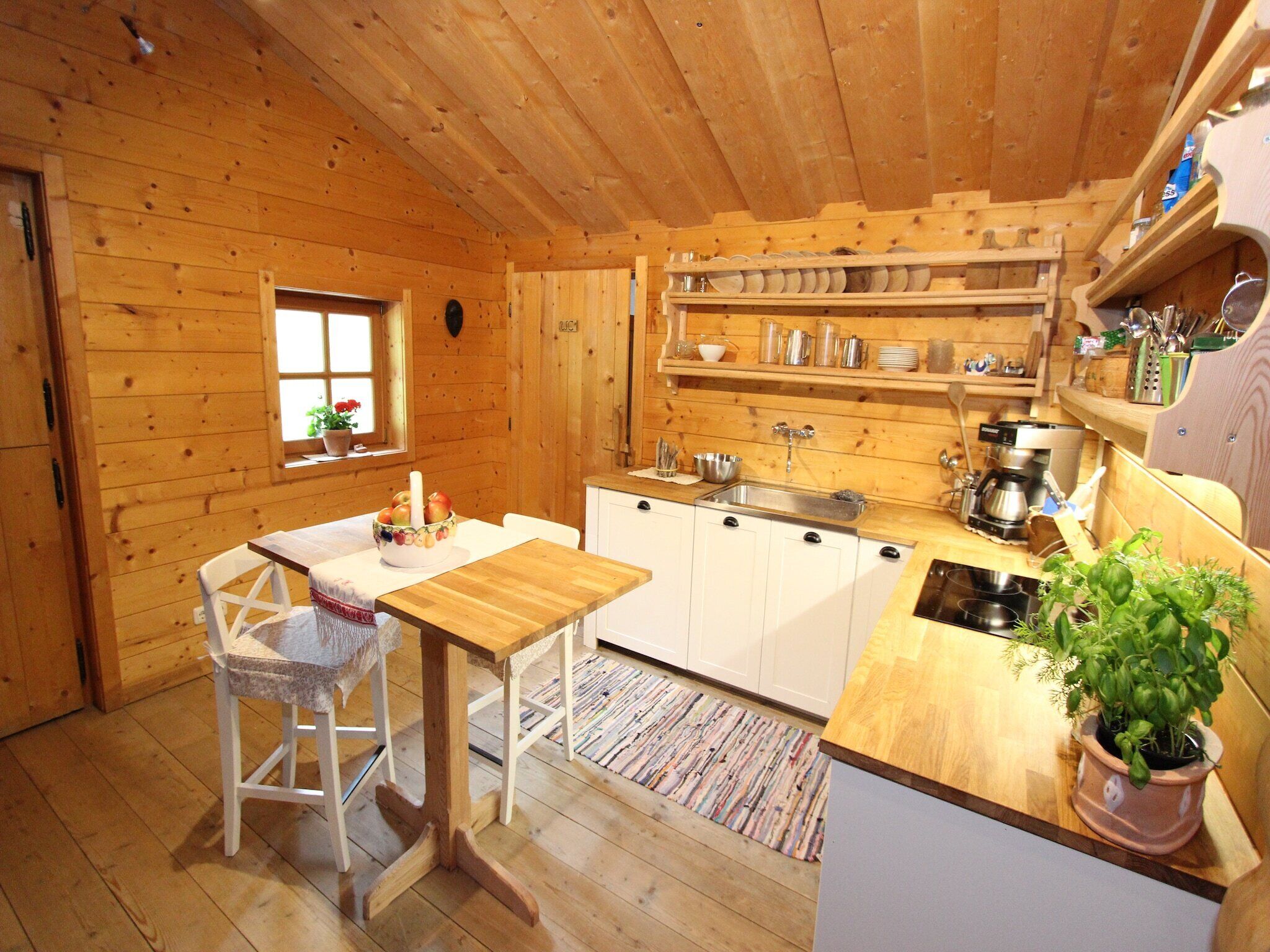 Een houten chalet met een keukenhoek, inclusief een tafel, stoelen, een spoelbak en een fornuis.