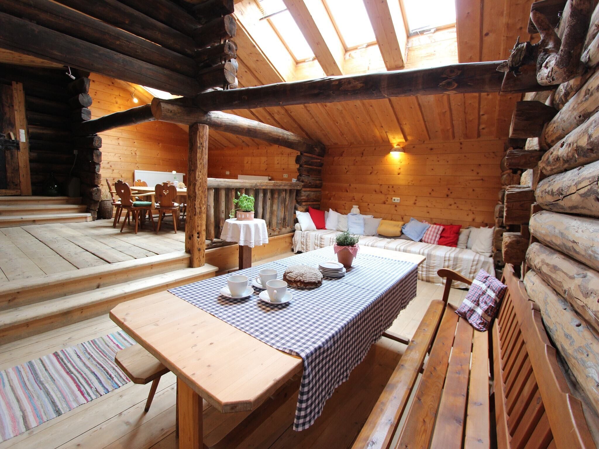Ein rustikaler Holzblockhaus-Innenraum mit einem Esstisch, der für vier Personen gedeckt ist, einer Couch mit Kissen und einer hölzernen Bank.