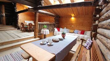 Ein rustikaler Holzblockhaus-Innenraum mit einem Esstisch, der für vier Personen gedeckt ist, einer Couch mit Kissen und einer hölzernen Bank.