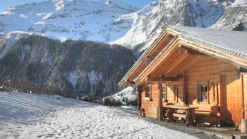 Eine Holzhütte mit Veranda vor einer verschneiten Berglandschaft.