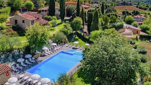 A pool area with lounge chairs and umbrellas, surrounded by greenery and buildings.