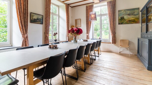 A dining area with a long table, black chairs, and a wooden floor.