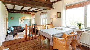 A cozy room with a wooden ceiling, a dining table with chairs, a sofa, and a window with a view.