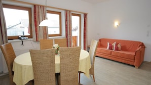 A dining area with wicker chairs and a table, a sofa, and a window with curtains. - Stylish Flats in Uderns near Ski Lift (Uderns)
