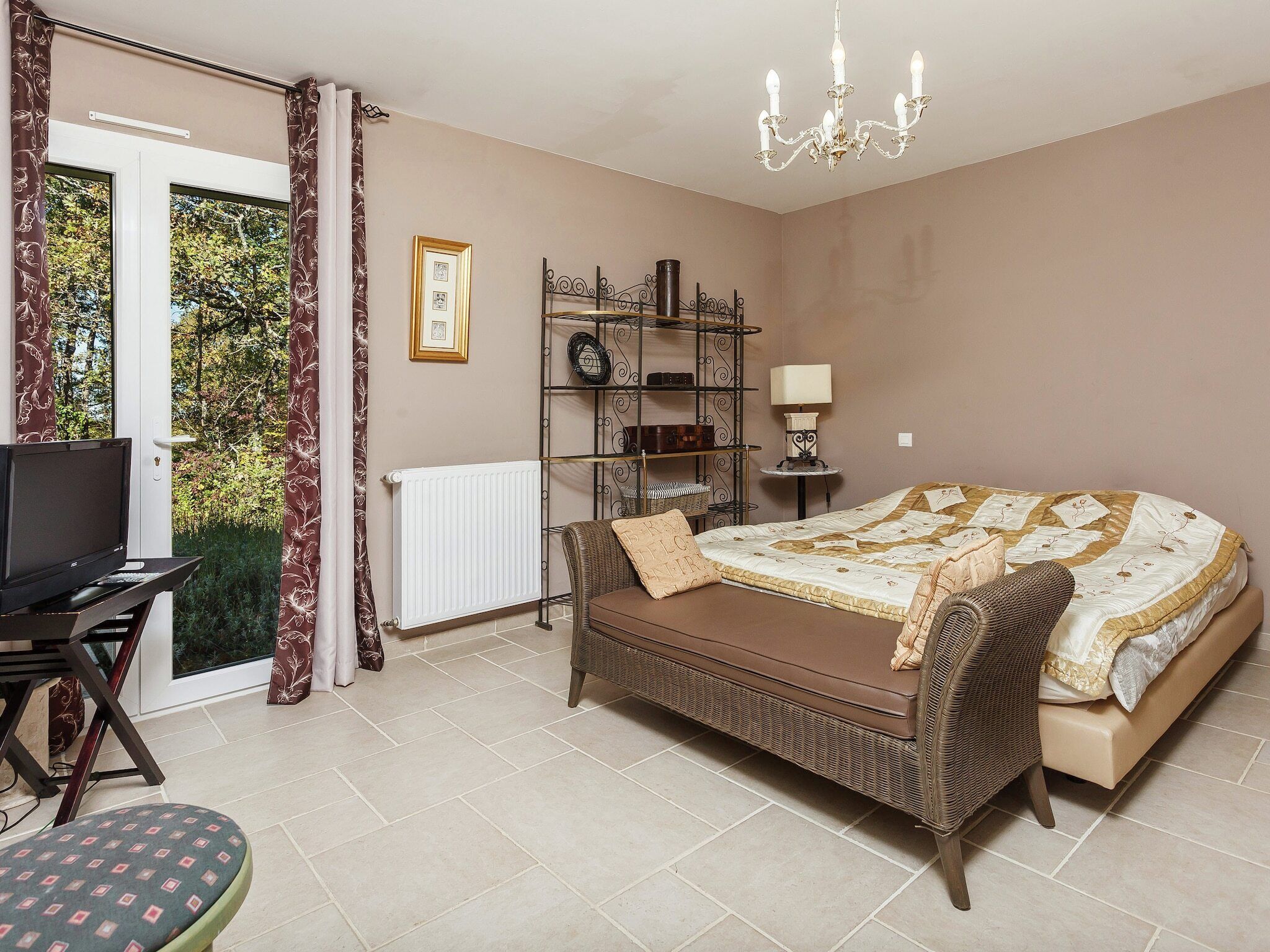 A bedroom with a bed, a television, a chair, a shelf with decorative items, and a window with curtains.