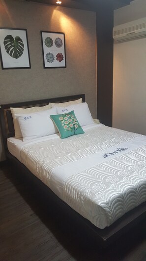 A neatly made bed with white bedding and a green pillow, a wall-mounted air conditioner, and two framed botanical prints above the bed. - Zen Motel (Nonsan)
