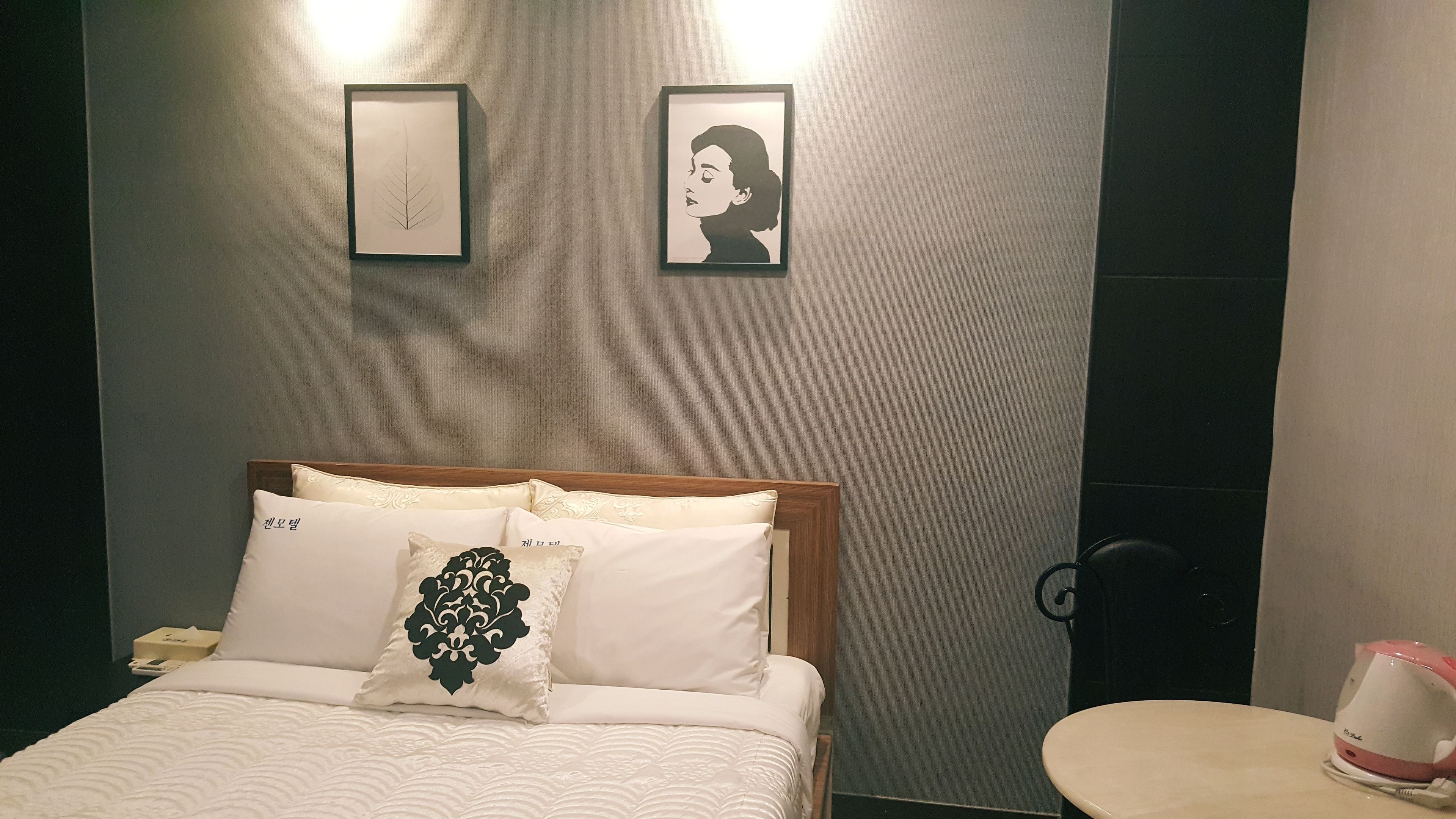 A hotel room with a bed, bedside table, and a wall-mounted kettle.