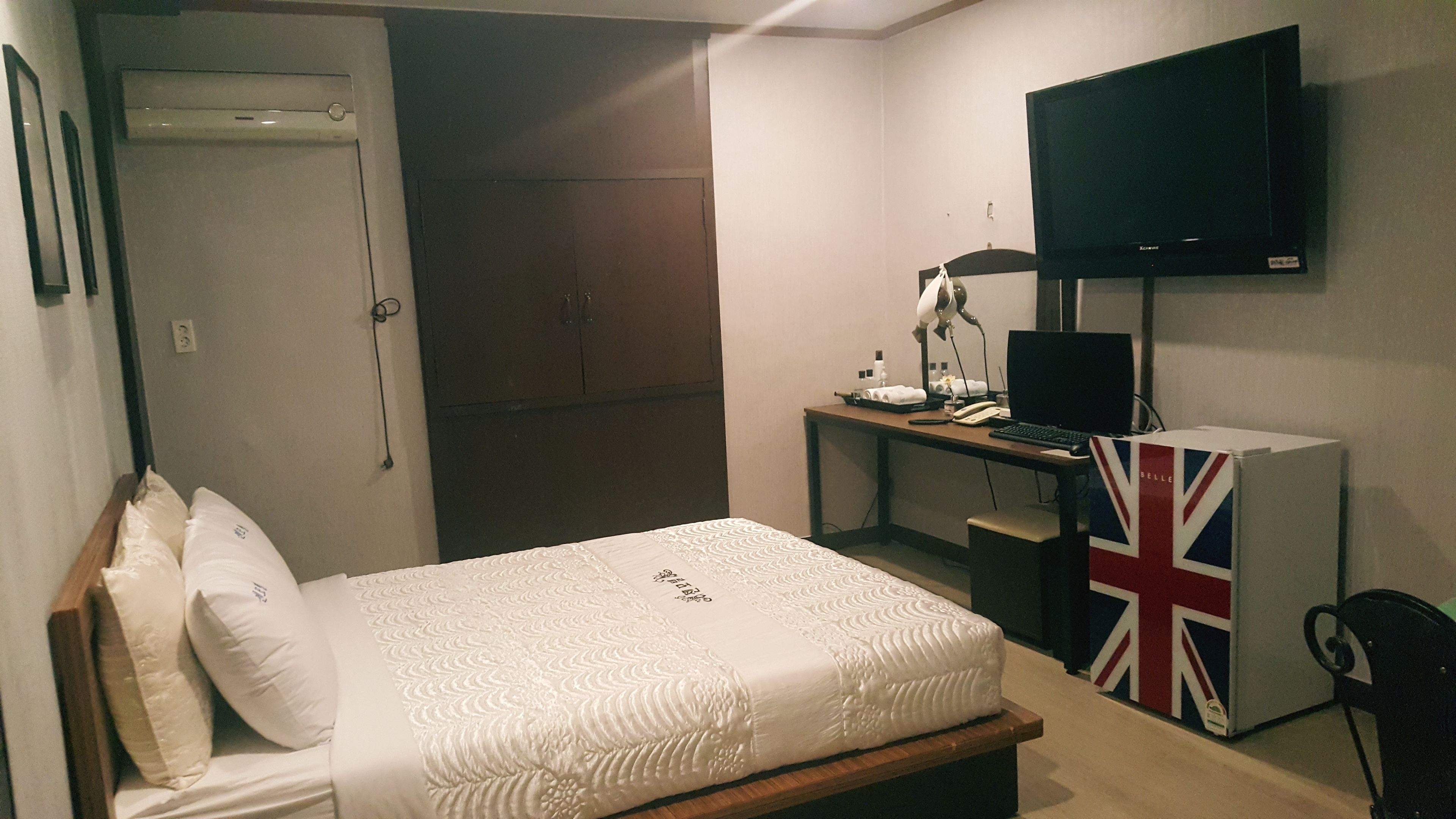 Un dormitorio con cama, escritorio, computadora, televisor y un refrigerador pequeño.