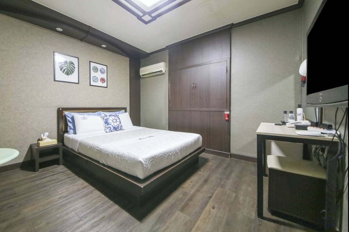 Une chambre à coucher comprenant un lit, une table de chevet, une commode, une armoire, un bureau, une chaise, un téléviseur et un climatiseur fixé au mur.